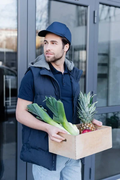 Молодий чоловік з доставкою тримає дерев'яну коробку зі свіжою їжею на відкритому повітрі — стокове фото