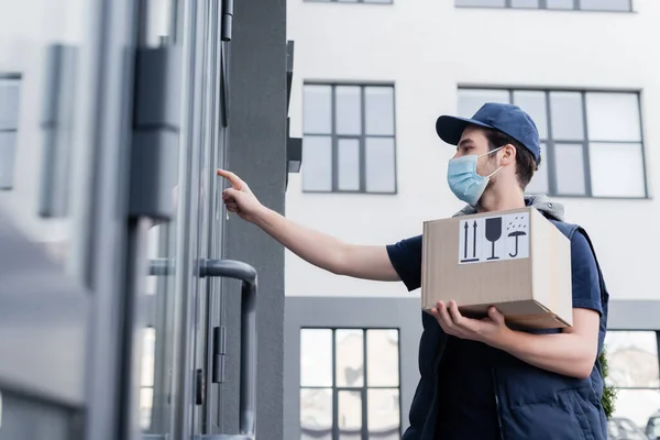 Low angle view of courier in medical mask holding package with signs near door of building outdoors — Photo de stock