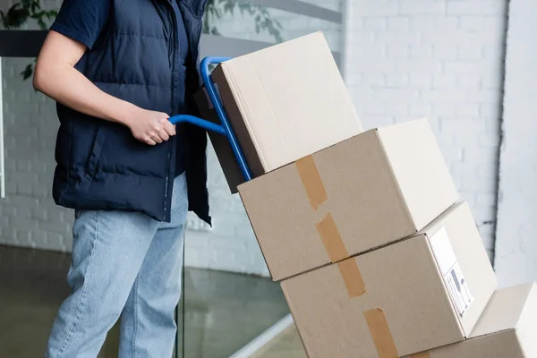 Cropped view of courier holding cart with packages in hallway — Stock Photo