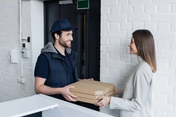 Усміхнений чоловік доставки, що сміє коробки для піци біля бізнес-леді в офісі — стокове фото