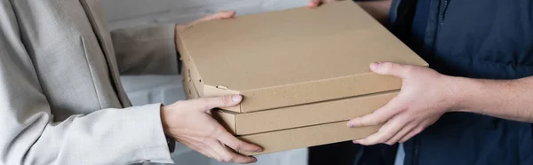 Cropped view of courier holding pizza boxes near businesswoman in office, banner — стоковое фото