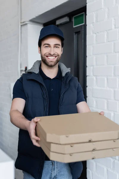 Positive courier holding blurred pizza boxes in hallway — стоковое фото