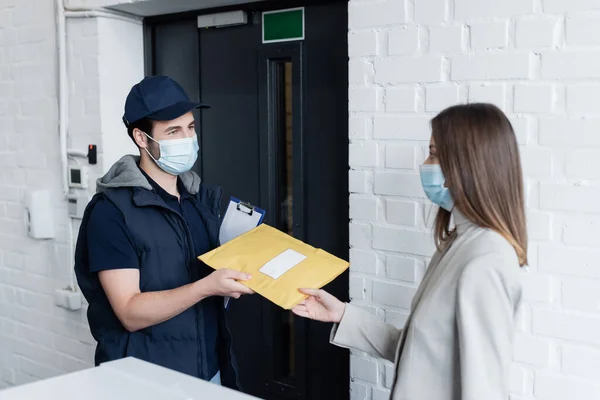 Courier in medical mask holding clipboard and parcel near businesswoman in office — Fotografia de Stock