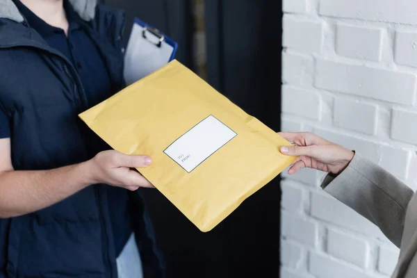 Cropped view of businesswoman taking parcel from courier with clipboard in office — стоковое фото