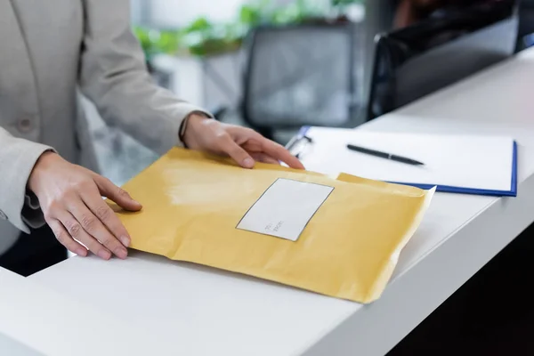 Cropped view of businesswoman taking parcel near blurred clipboard in office — стоковое фото