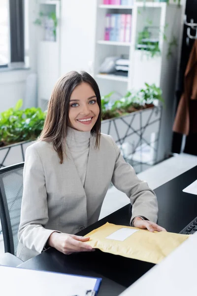 Smiling businesswoman holding parcel and looking at camera in office — стоковое фото