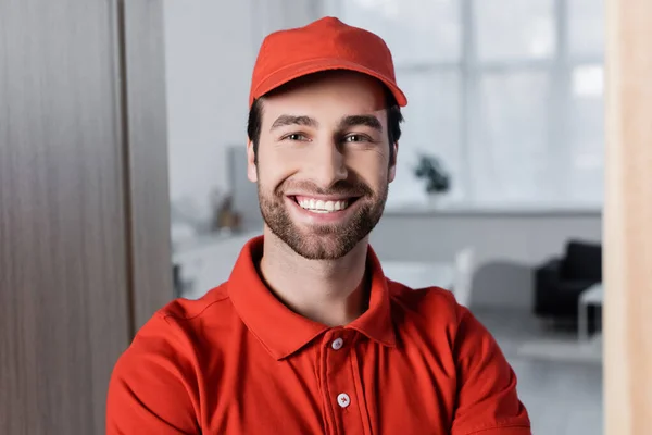 Positive courier in uniform smiling at camera in hallway — стоковое фото