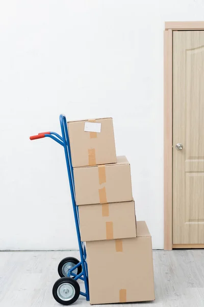 Cardboard boxes on cart near door in hallway - foto de stock