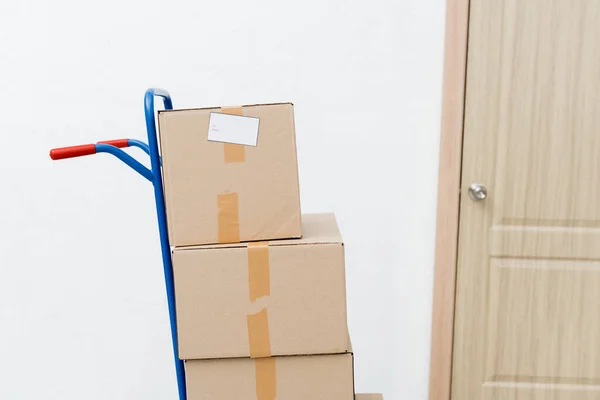 Carton boxes on cart near door in hallway — Stock Photo