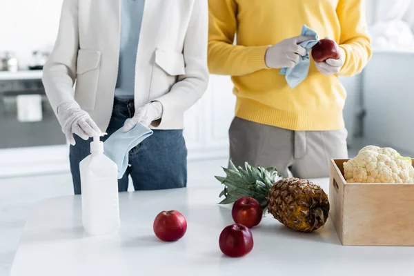 Cropped view of couple in latex gloves cleaning fresh food with antiseptic near box in kitchen — Photo de stock