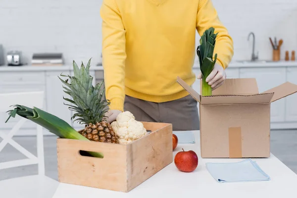 Cropped view of man in latex gloves taking fresh food near boxes and rags in kitchen — Stock Photo