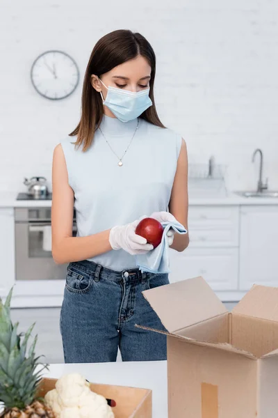 Woman in medical mask cleaning apple near boxes in kitchen — Foto stock