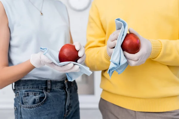 Cropped view of blurred couple in latex gloves cleaning apples in kitchen — Stock Photo