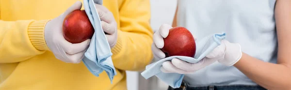 Cropped view of woman in latex gloves cleaning apple with rag near boyfriend at home, banner — Foto stock
