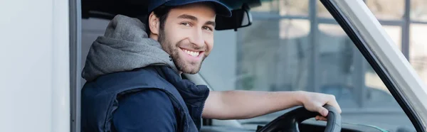 Позитивний чоловік доставки посміхається на камеру під час водіння автомобіля, банер — стокове фото