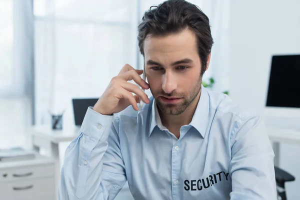 Guard in shirt with security lettering talking on mobile phone in office — Stock Photo