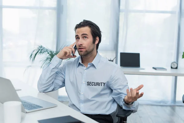 Security man gesturing while talking on mobile phone in supervision room — Stock Photo