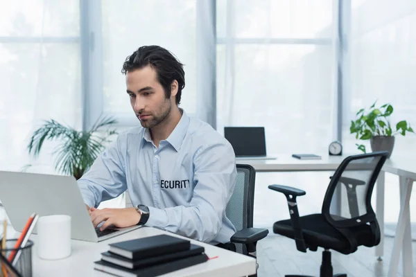 Junger Security-Mann tippt im Überwachungsraum auf Laptop — Stockfoto