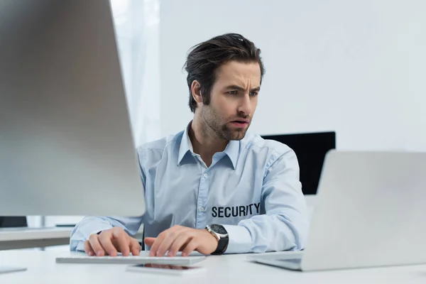 Uomo di sicurezza premuroso guardando computer portatile mentre digita sulla tastiera del computer in ufficio — Foto stock