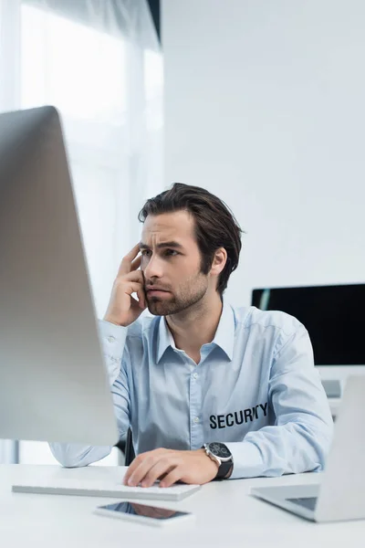 Seriöser Sicherheitsmann blickt auf verschwommenen Computermonitor im Überwachungsraum — Stockfoto