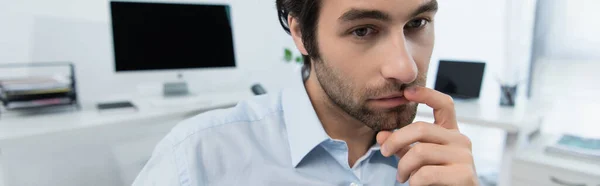 Стомлений бізнесмен торкається губ, думаючи біля комп'ютерів на розмитому фоні, банер — стокове фото