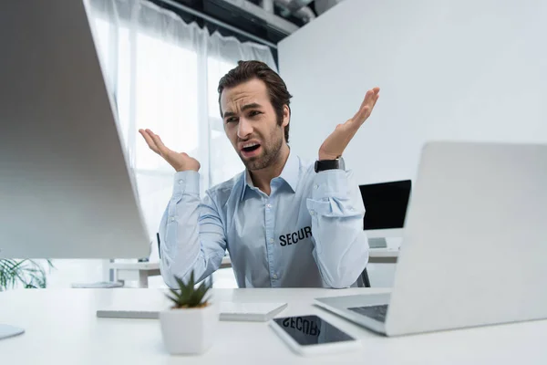 Homem de segurança descontente gesticulando perto de monitor de computador e laptop no escritório — Fotografia de Stock