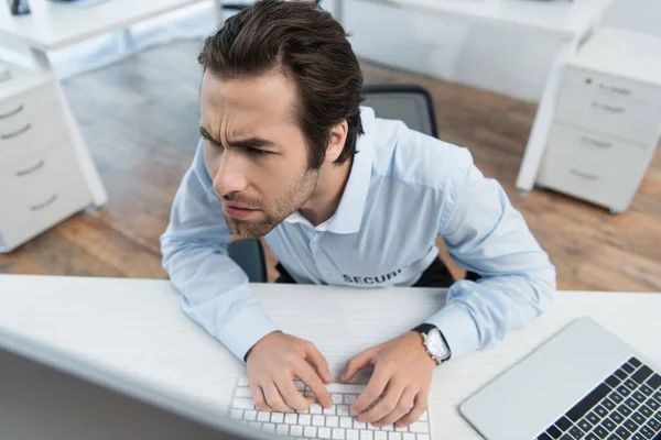 Vista de ángulo alto del tenso hombre de seguridad mirando el monitor de la computadora en la sala de vigilancia - foto de stock