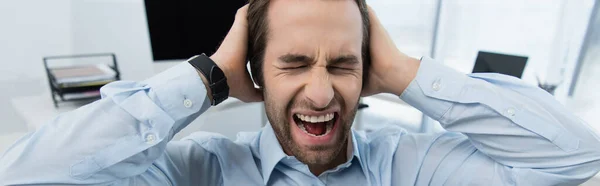 Hombre de seguridad enojado con los ojos cerrados tocando la cabeza mientras grita en la oficina, pancarta - foto de stock