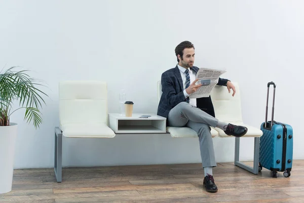 Vista completa del hombre leyendo el periódico en la sala de salida cerca de maleta y café para ir — Stock Photo