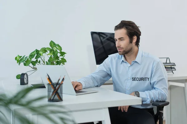 Homem de segurança em uniforme usando laptop enquanto trabalhava na sala de supervisão — Fotografia de Stock