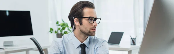 Hombre de seguridad concentrado trabajando cerca de computadoras borrosas en la sala de supervisión, pancarta - foto de stock