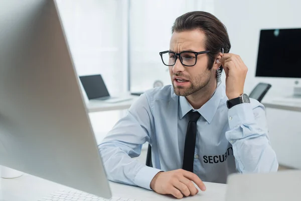 Wachmann mit Brille und Kopfhörer blickt auf Computermonitor im Sicherheitsraum — Stockfoto