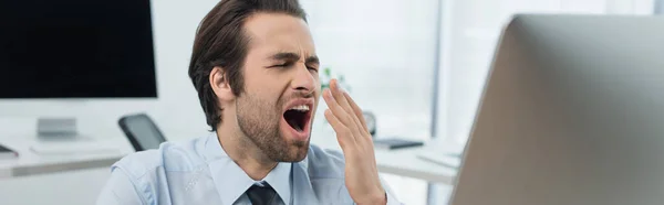 Sleepy guard covering mouth with hand while yawning near blurred monitors, banner — Stock Photo