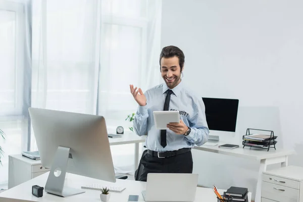 Fröhlicher Sicherheitsmann gestikuliert beim Blick auf digitales Tablet im Überwachungsraum — Stockfoto