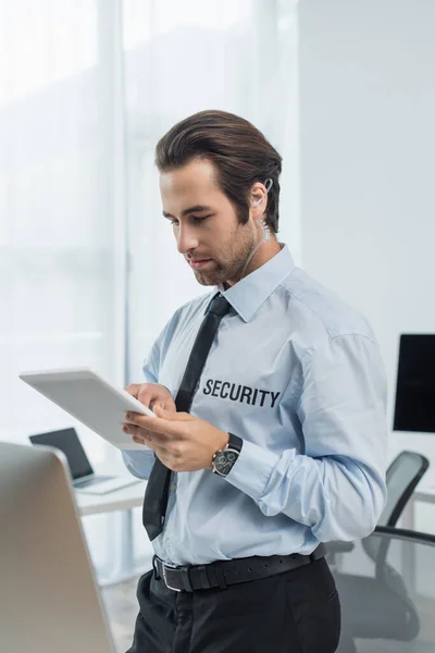 Guard in earphone and shirt with security lettering using digital tablet in office — Stock Photo