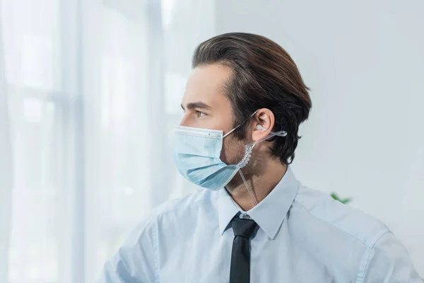 Young security man in earphone and medical mask looking away in office — Stock Photo