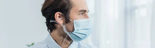 Hombre de seguridad en máscara médica y auriculares mirando hacia otro lado en la oficina, pancarta - foto de stock
