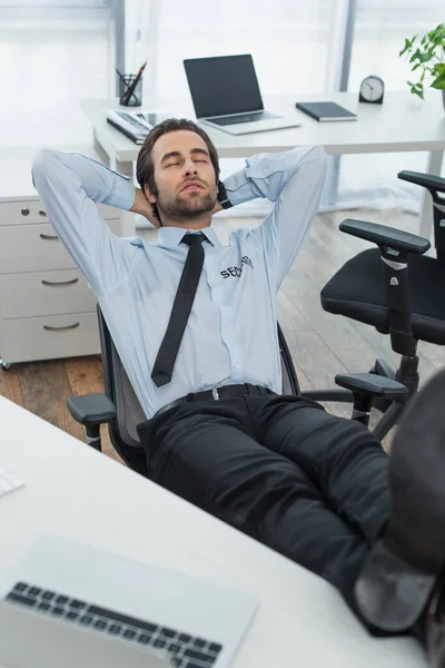 Hombre de seguridad sentado con las piernas en el escritorio y durmiendo en la oficina - foto de stock