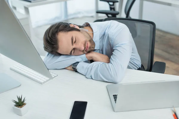 Erschöpfter Sicherheitsmann schläft am Arbeitsplatz in der Nähe von Laptop, Monitor und Smartphone mit leerem Bildschirm — Stockfoto