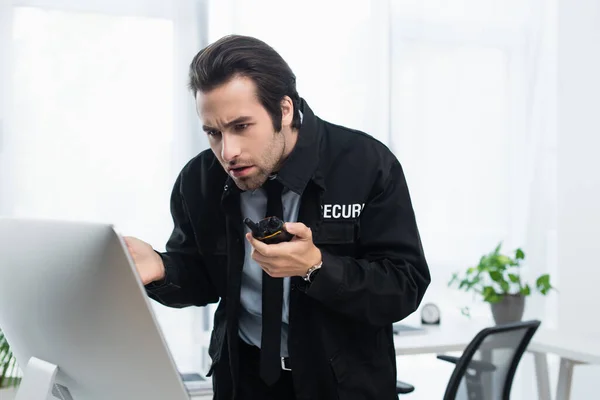 Worried security man with walkie-talkie looking at computer monitor in office — Stock Photo