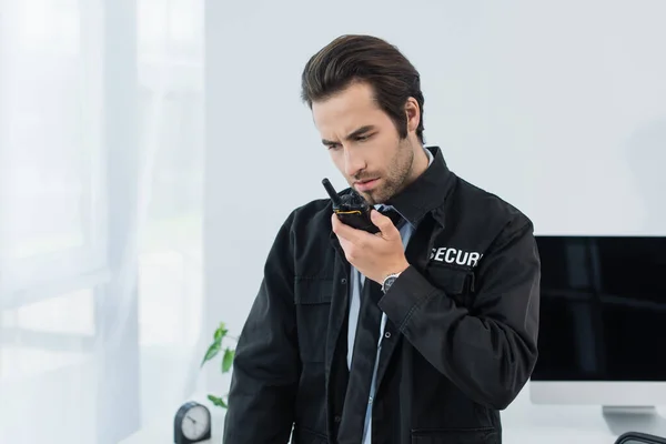 Serio uomo di sicurezza in uniforme nera che chiama walkie-talkie in ufficio — Foto stock
