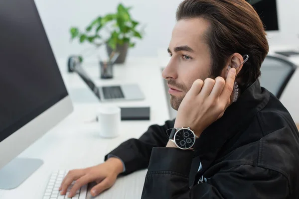Serious security man touching earphone while working in supervision room — Stock Photo