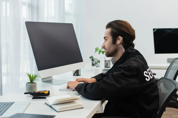 Wachmann in Uniform und Kopfhörertippen am Computer in der Nähe von Walkie-Talkie und Notizbuch — Stockfoto