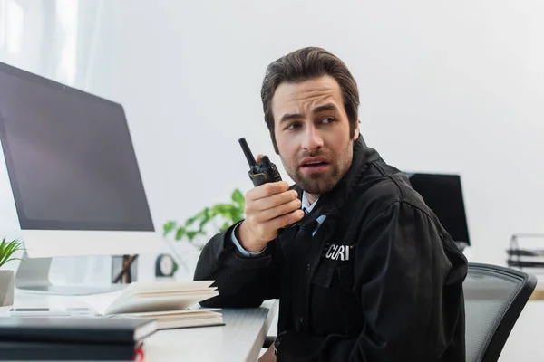 Sicherheitsmann spricht auf Walkie-Talkie in der Nähe verschwommener Monitore im Überwachungsraum — Stockfoto