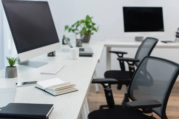 Desks with computer monitors, blurred laptop and notebooks near office chairs — Stock Photo