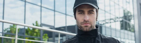 Young security man in black cap looking at camera outdoors, banner — Stock Photo