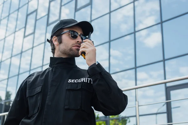 Uomo di sicurezza in occhiali da sole e uniforme nera che parla alla radio all'aperto — Foto stock