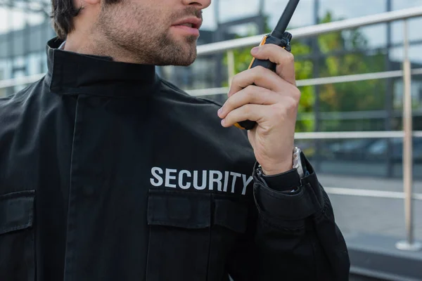 Vista parcial del guardia en uniforme con letras de seguridad hablando en walkie-talkie al aire libre - foto de stock