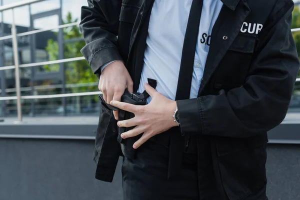 Обрезанный вид охранника, вынимающего пистолет из кобуры на городской улице — стоковое фото
