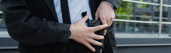 Partial view of security man taking gun out of holster outdoors, banner — Stock Photo